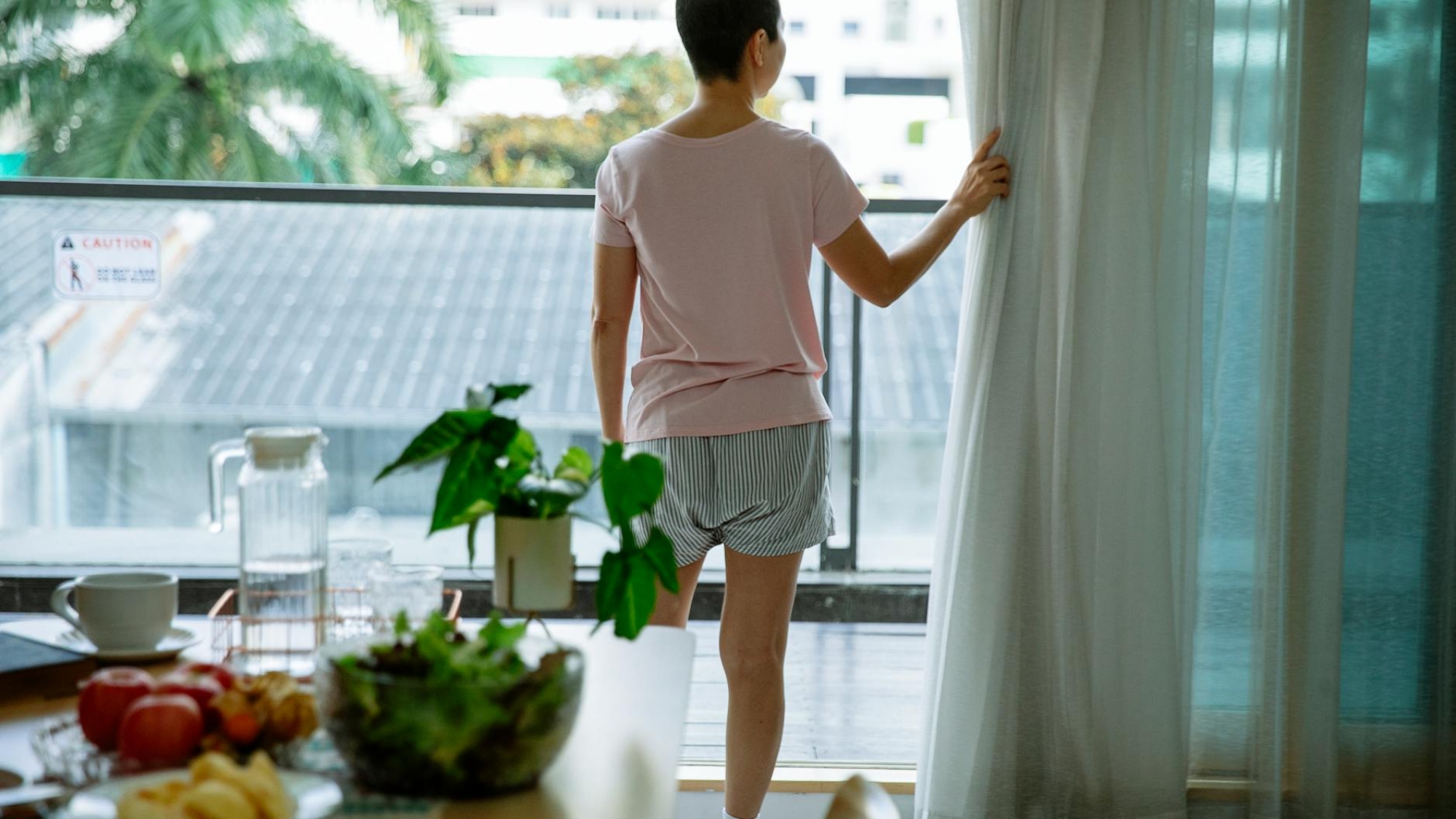 short haired sick woman opening curtain of window in hospital