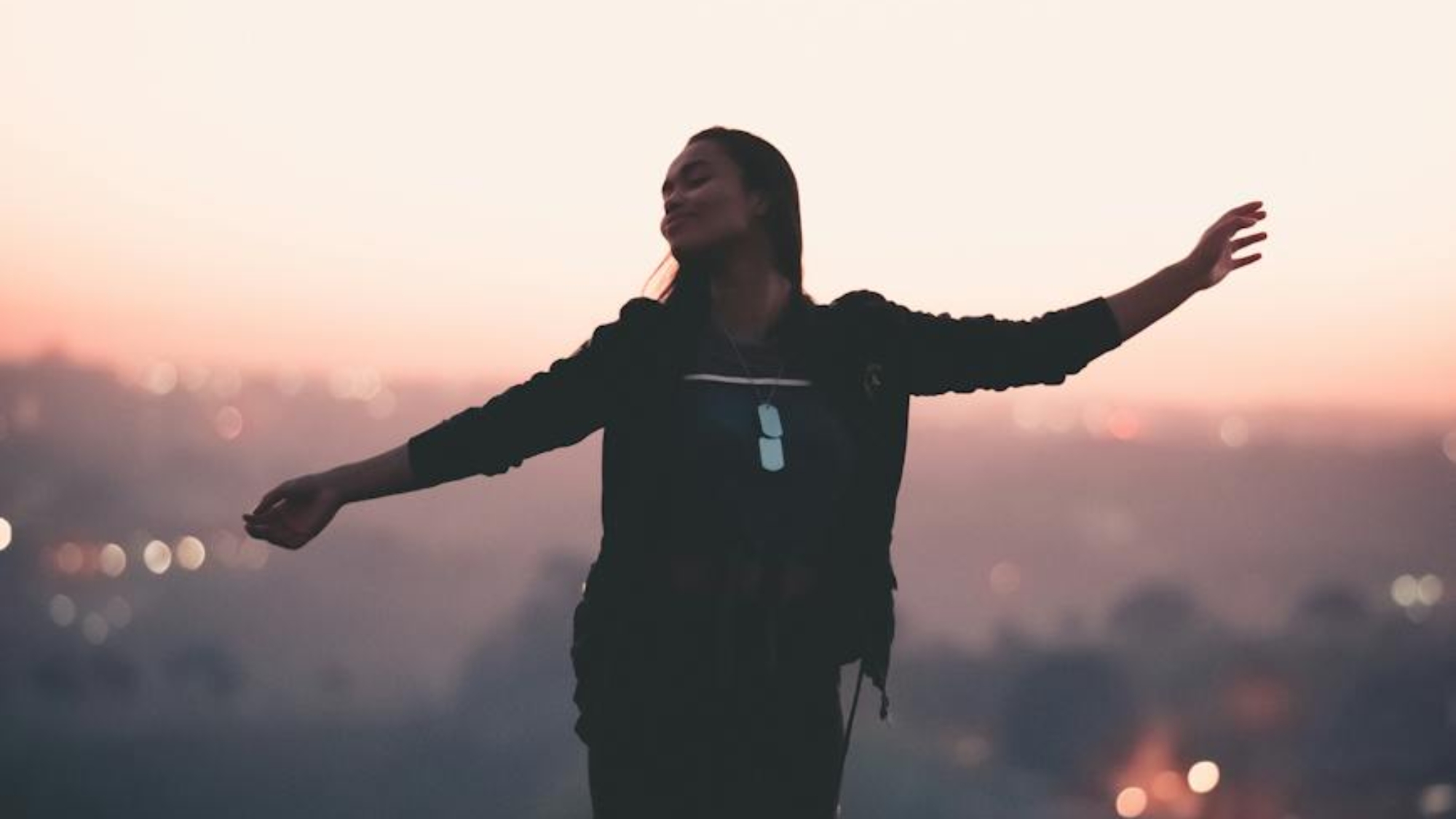 happy black woman with arms apart on top of mountain at sunset