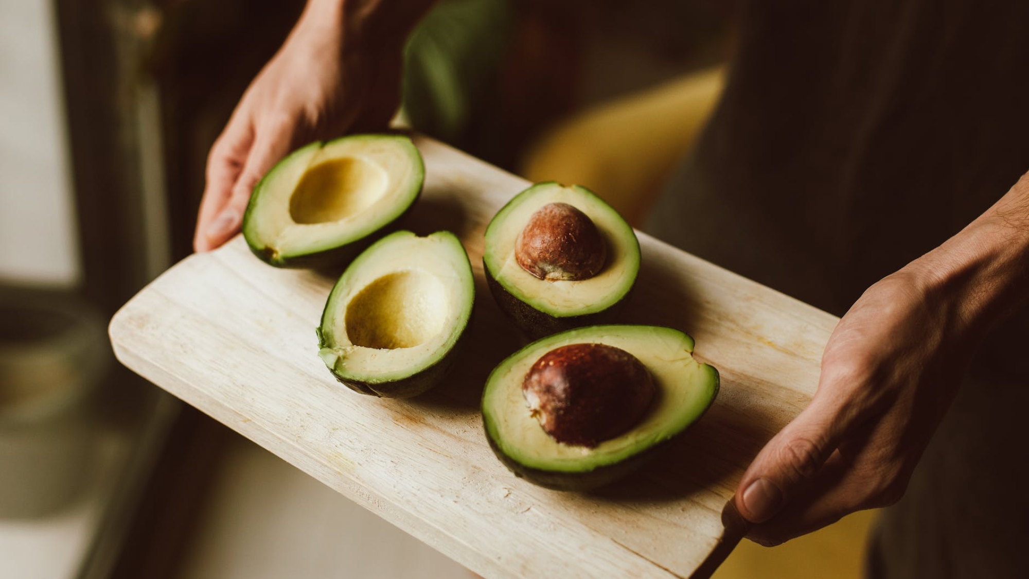 close up shot of a person holding a wooden tray with sliced avocados