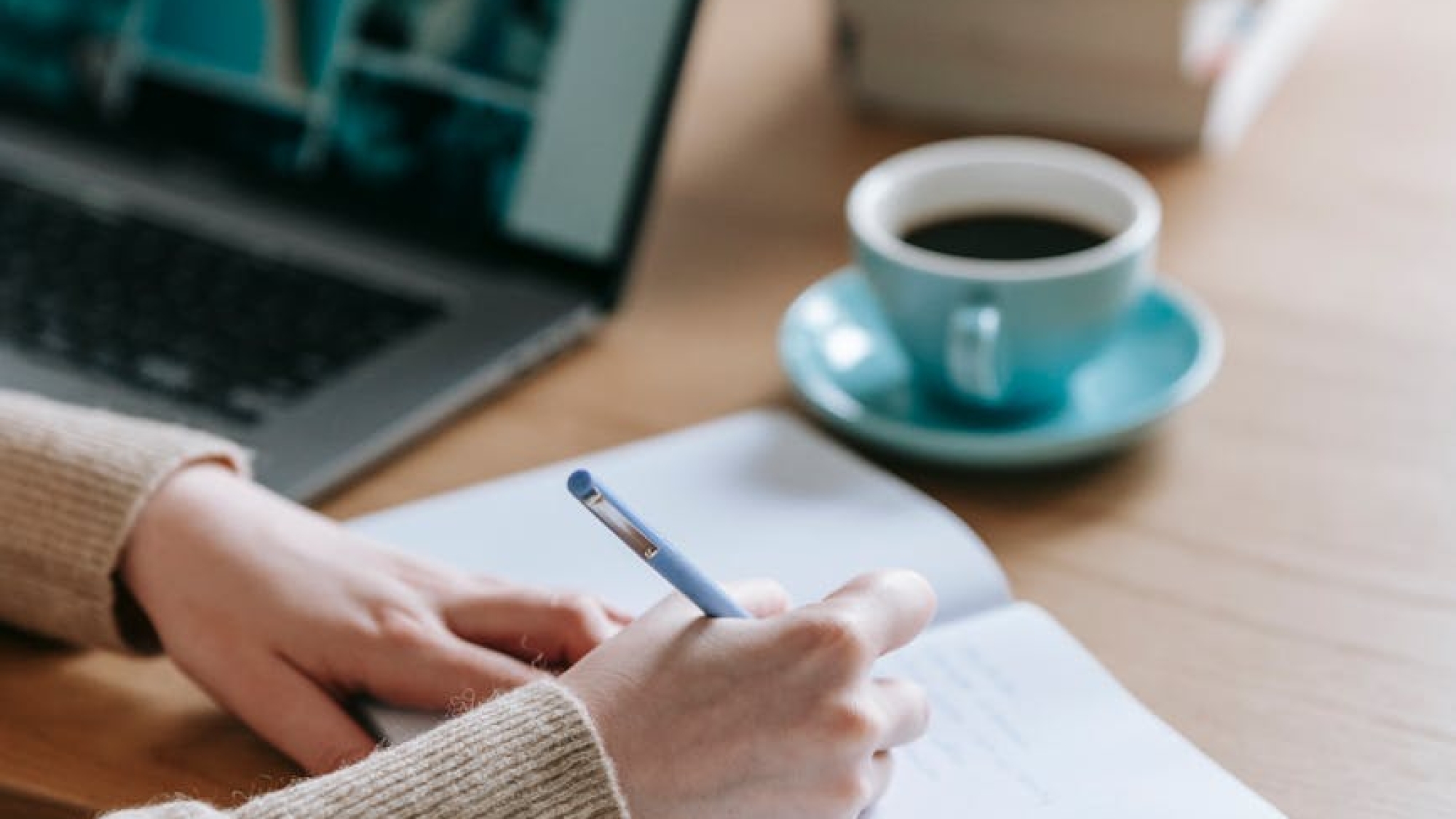businesswoman writing thoughts in empty notebook near laptop and coffee