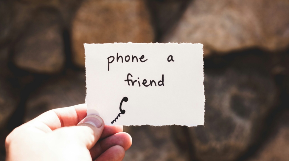 person holding piece of paper with phone a friend written text